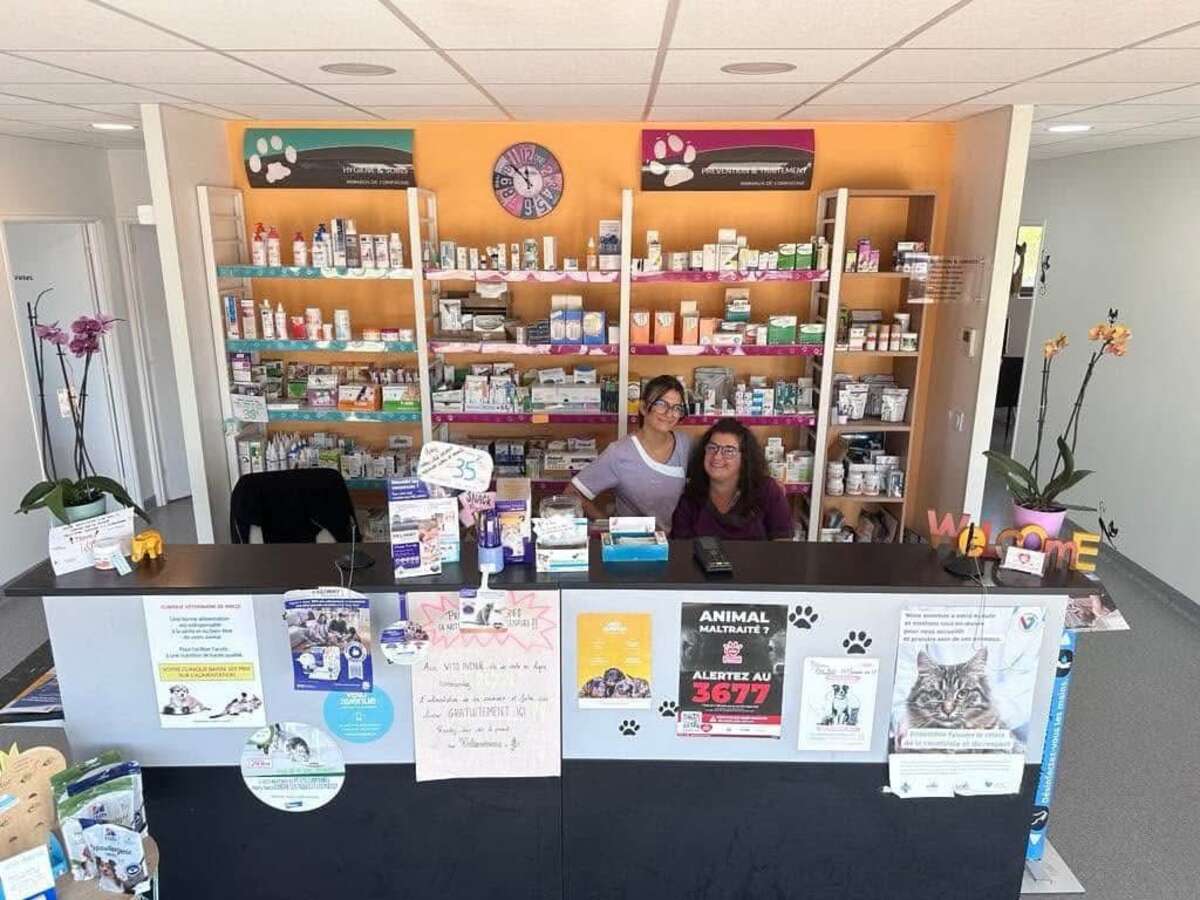 Bureau d’accueil de la clinique vétérinaire de Riscle Bureau d’accueil de la clinique vétérinaire de Riscle avec deux ASV souriantes devant des étagères remplies de médicaments